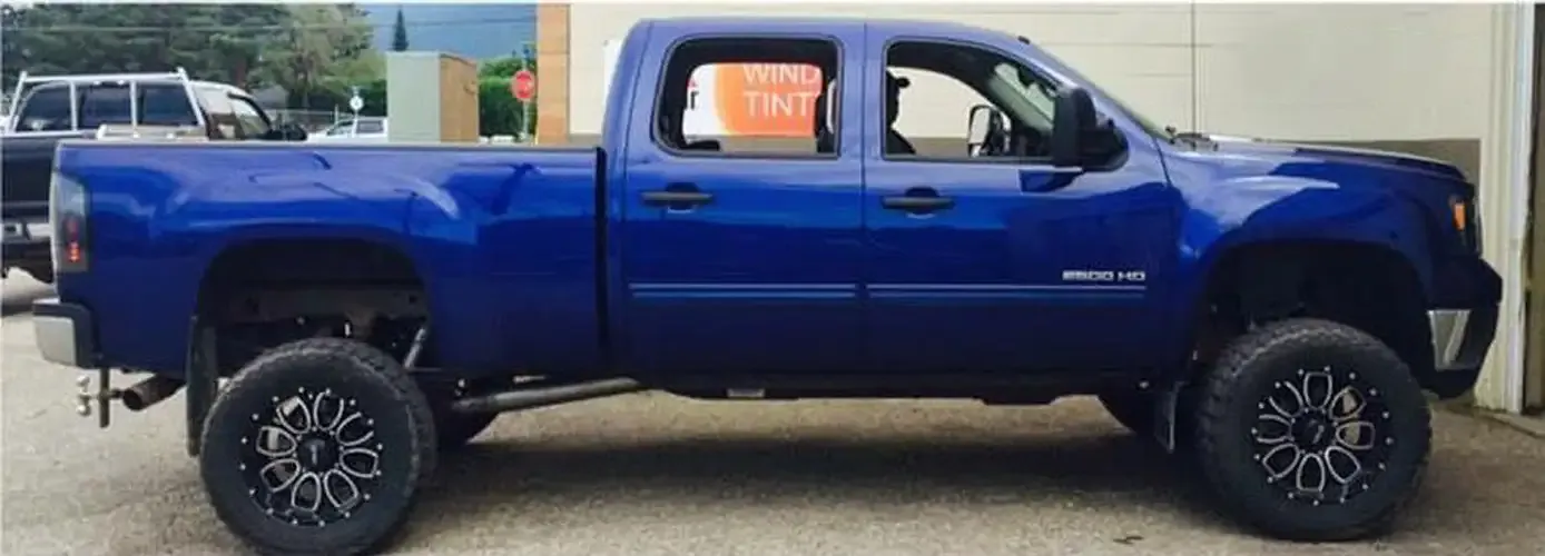 Lifted blue GMC 2500HD with fresh window tint outside the Graphic Enterprises shop